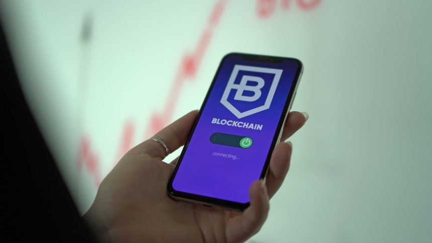Mão segurando um smartphone que exibe uma carteira digital de criptomoedas baseada em blockchain.