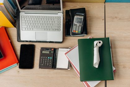 Mesa de escritório organizada com laptop, calculadora, terminal de pagamento e documentos.