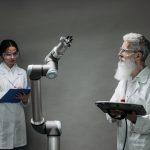 Dois pesquisadores analisam um braço robótico em um laboratório de tecnologia.