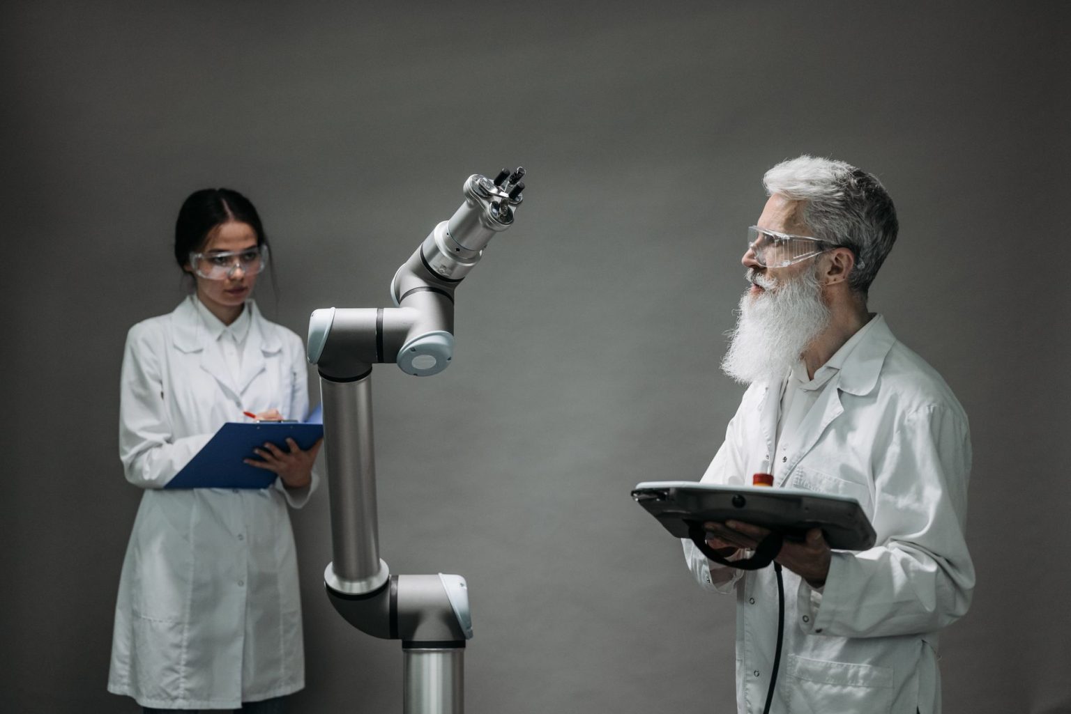 Dois pesquisadores analisam um braço robótico em um laboratório de tecnologia.